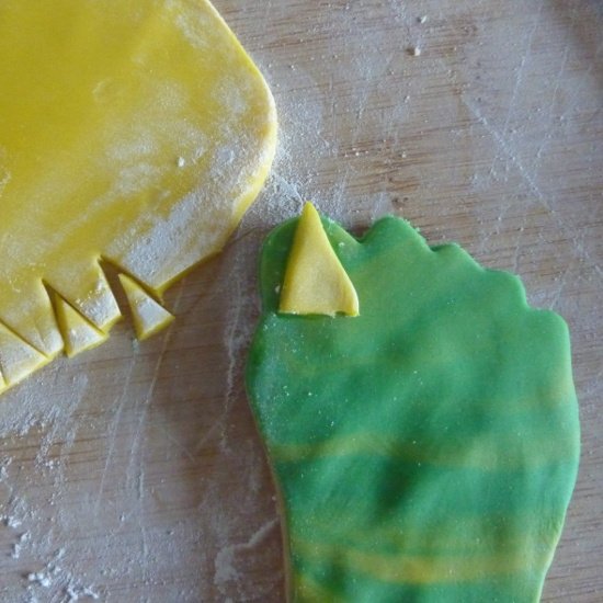 Making shaped zombie feet using colored rolled fondant adding yellow rolled fondant on to green fondant feet