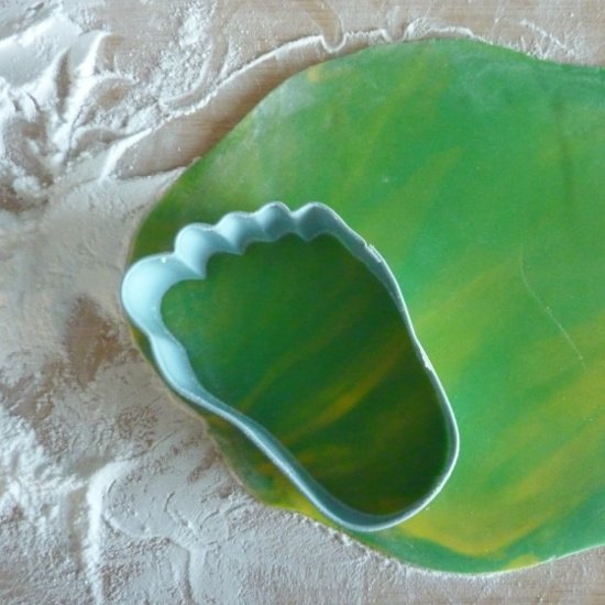 Cutting out colored green yellow rolled fondant icing with a cutter using a shaped foot feet cookie cutter to cut green rolled fondant icing