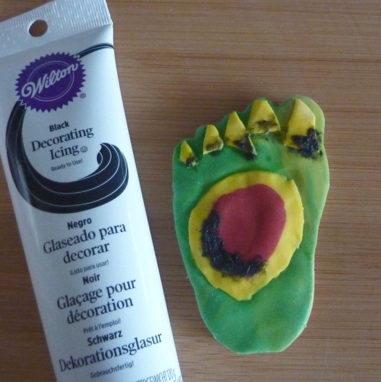 Adding final detail to the zombie cookies black color on the body part cookie feet adding black decorating squeeze tube icing onto Halloween cookies