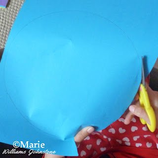 child cutting out a blue circle of paper with kid friendly scissors