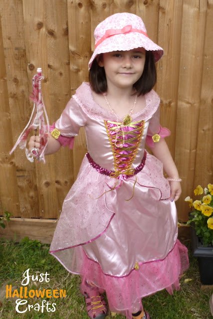 Girl dressed up in a pale pink princess costume with matching hat and wand