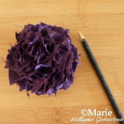 Purple satin fabric pom pom and a black cord wrapped stick