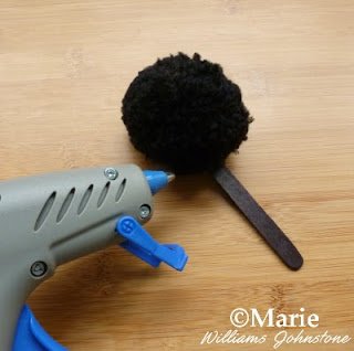Hot glue gun used to stick a black yarn pom pom onto a popsicle stick