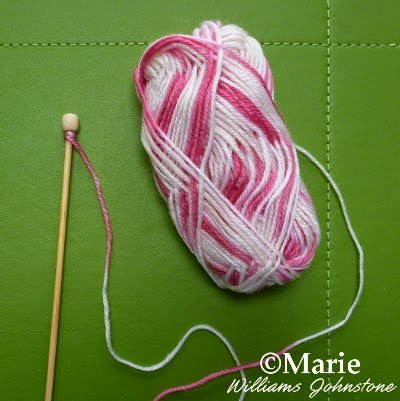 Variegated pink candy yarn wrapped around wooden knitting needle