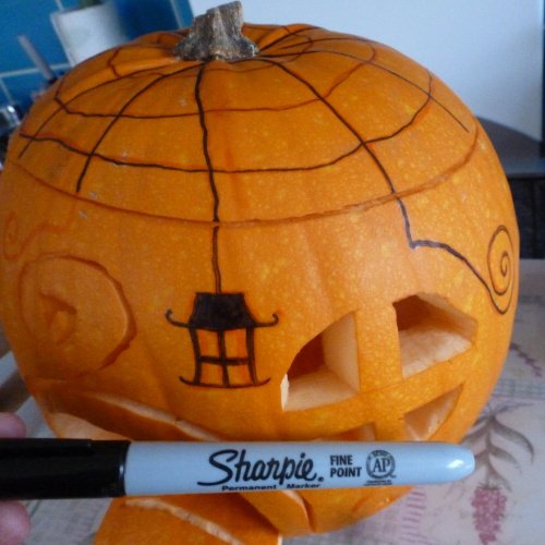 Black pen designs drawing onto pumpkin lid with spider web cobweb
