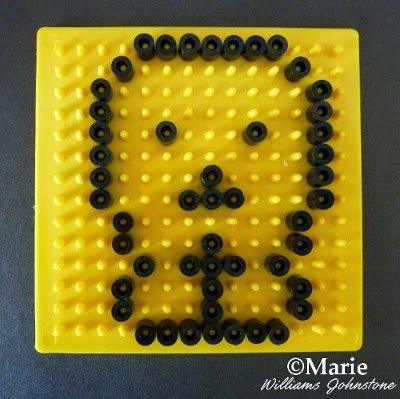 Yellow pegboard with beads outlining shape of a skull