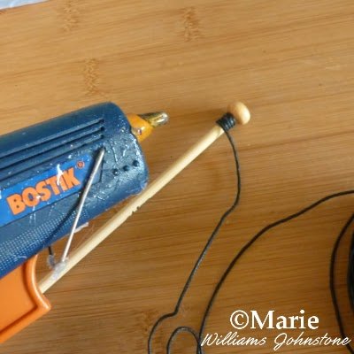 Wrapping black cord around a wooden stick with adhesive
